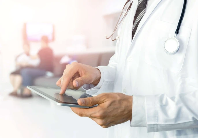 A doctor holding a tablet while patients wait in the background