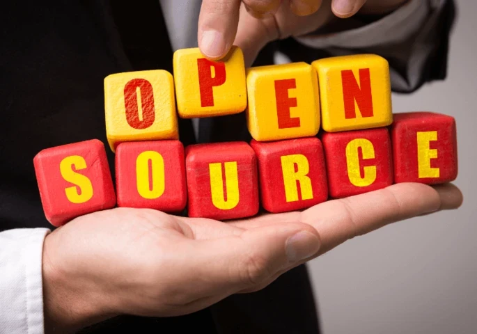 The words "Open Source" on red and yellow blocks held by a person in a suit.