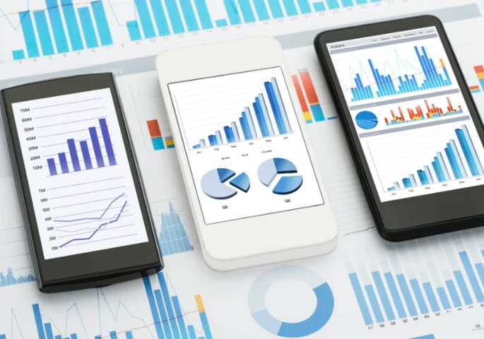 Three smartphone laid on top of a pile of paper graphs.