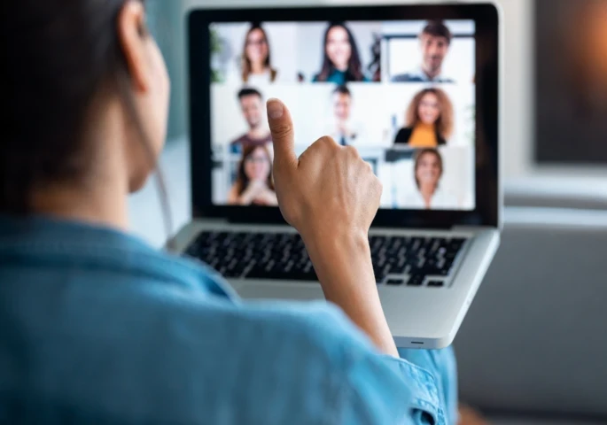 A woman sitting in front of a laptop on a video meeting giving a thumbs up.