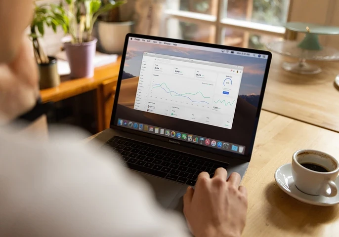 Person sitting at a desk working on a laptop with graphs on the screen.