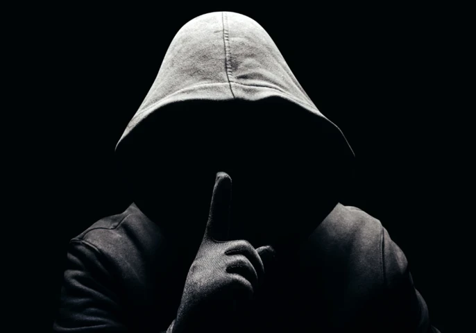 A person in a black hoodie holding up his finger to his mouth.