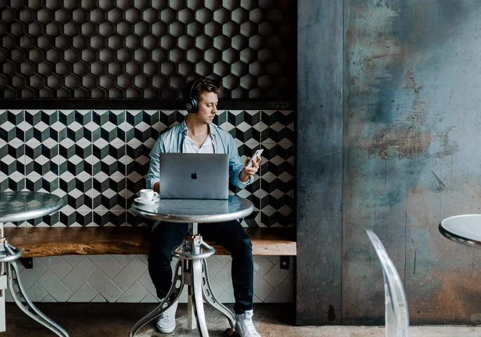 Man sitting in a cafe working on his laptop and holding a smartphone.