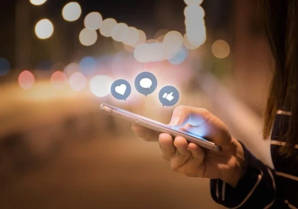 Person using a smartphone with Facebook reaction emojis floating above the screen