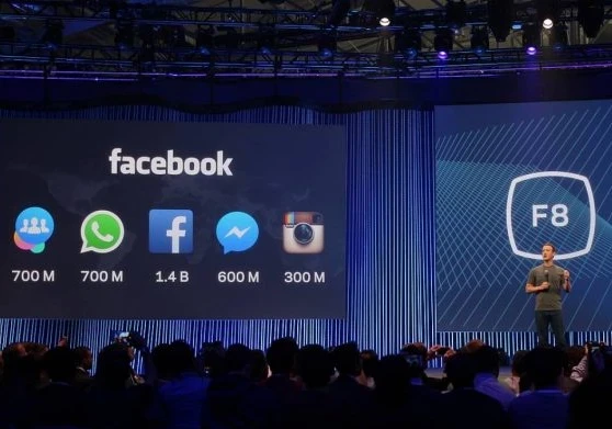 Mark Zuckerberg on stage presenting with the Facebook logo behind him.