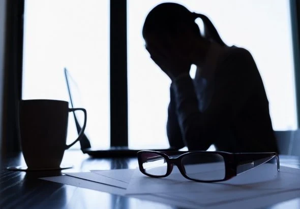 Woman sitting at a desk with her head in her hands.