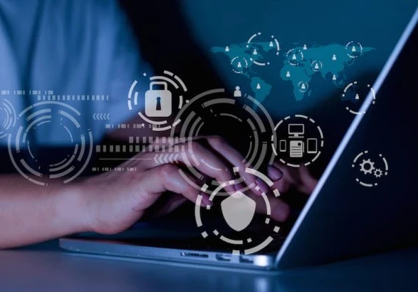 A close up of hands typing on a laptop with security icons floating around.