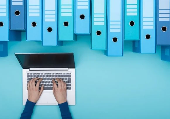 A person working on a laptop with large files and folders hanging above