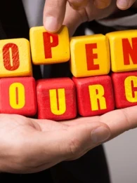 The words "Open Source" on red and yellow blocks held by a person in a suit.