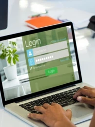 A woman sitting in front of a laptop with a login screen displayed.