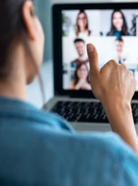 A woman sitting in front of a laptop on a video meeting giving a thumbs up.