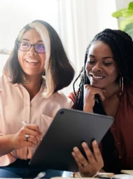 A group of four women sitting at a desk, invested in a discussion around a tablet.