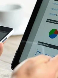 Person using a smartphone and pointing at a screen with charts on it.