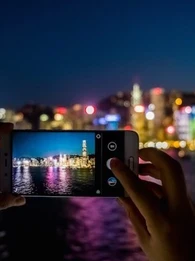 Person taking a photo using a smartphone of a China city skyline across the river at night