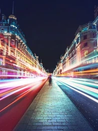 Person walking down Oxford Street with lights beaming past on either side