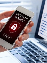Person holding a smartphone with the words "Security Breach" and a lock in front of a laptop displaying graphs.
