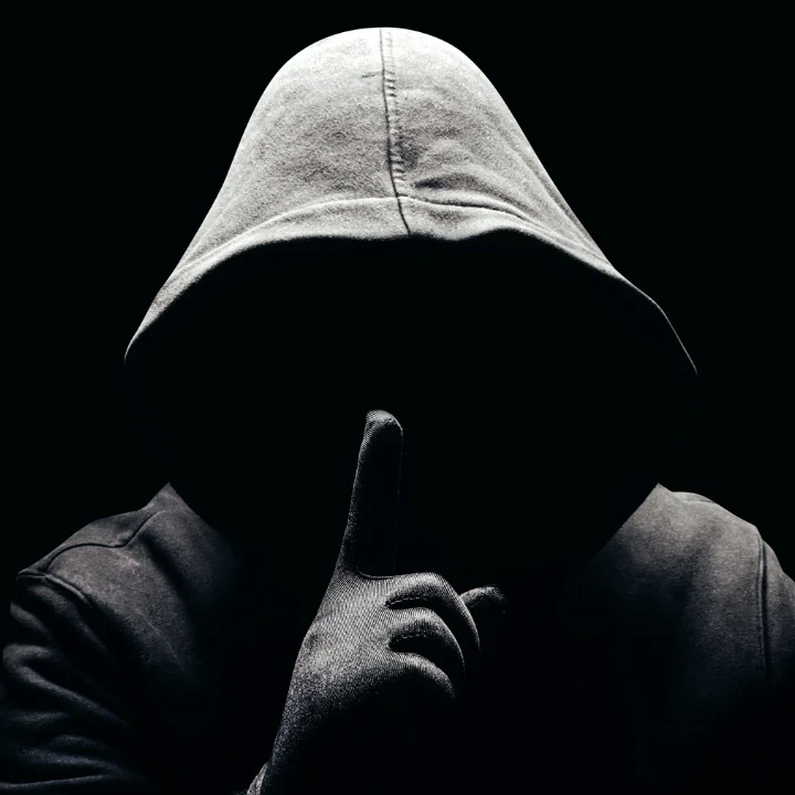 A person in a black hoodie holding up his finger to his mouth.