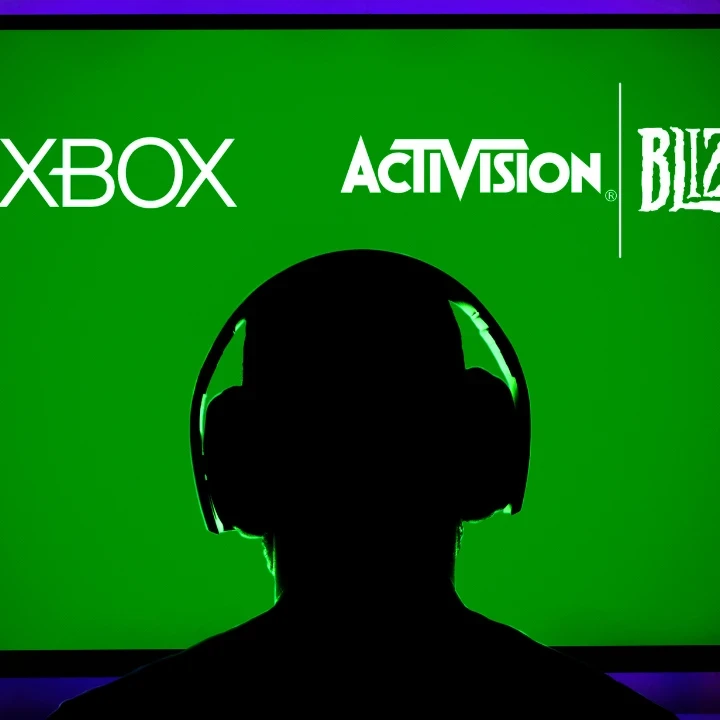 Silhouette of a person with headphones on in front of a green TV screen displaying logos from XBox, Activision and Blizzard.