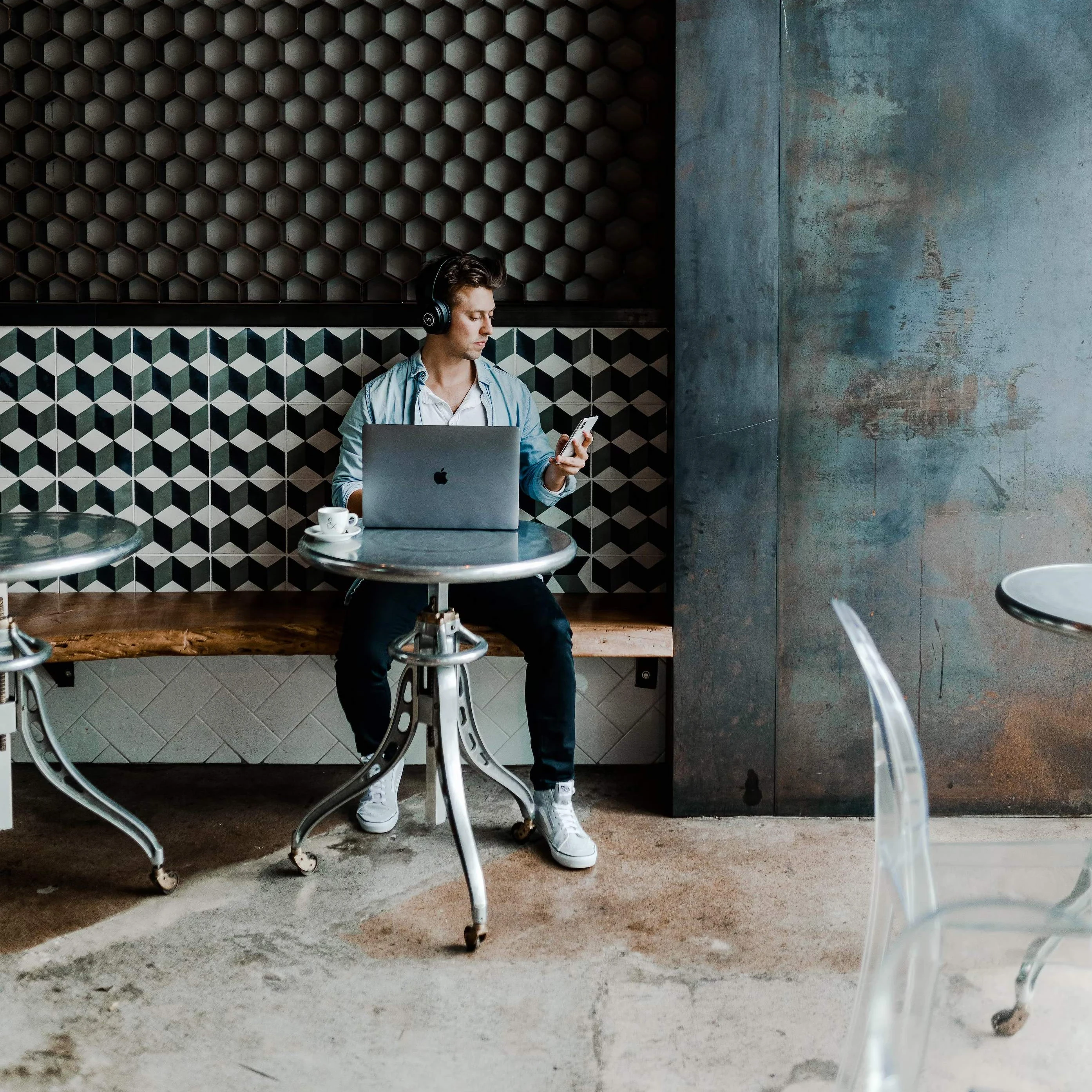 Man sitting in a cafe working on his laptop and holding a smartphone.
