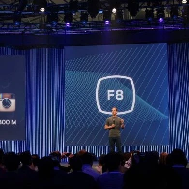 Mark Zuckerberg on stage presenting with the Facebook logo behind him.