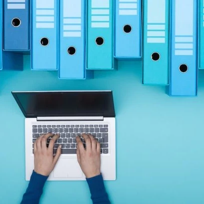 A person working on a laptop with large files and folders hanging above
